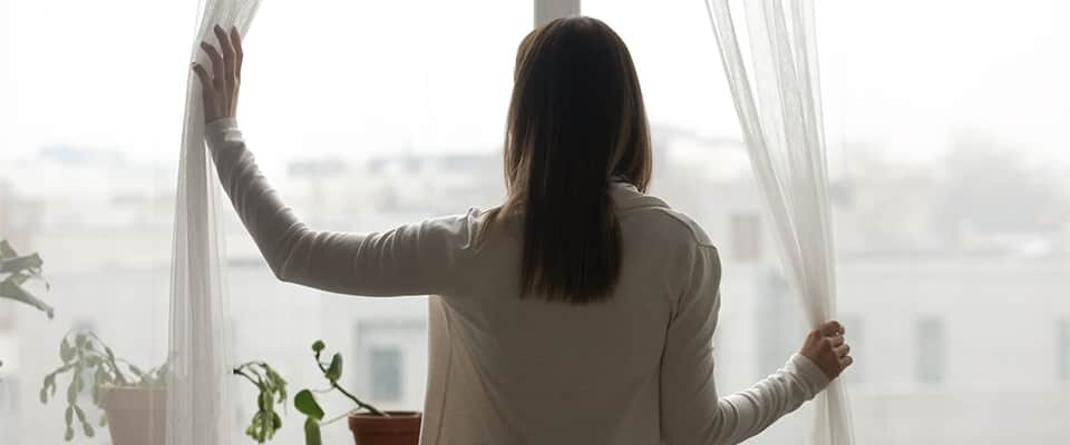 A woman stands in front of a window with the curtains drawn