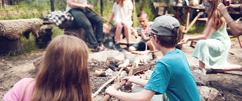 Kinder sitzen mit Stockteig an Lagerfeuer